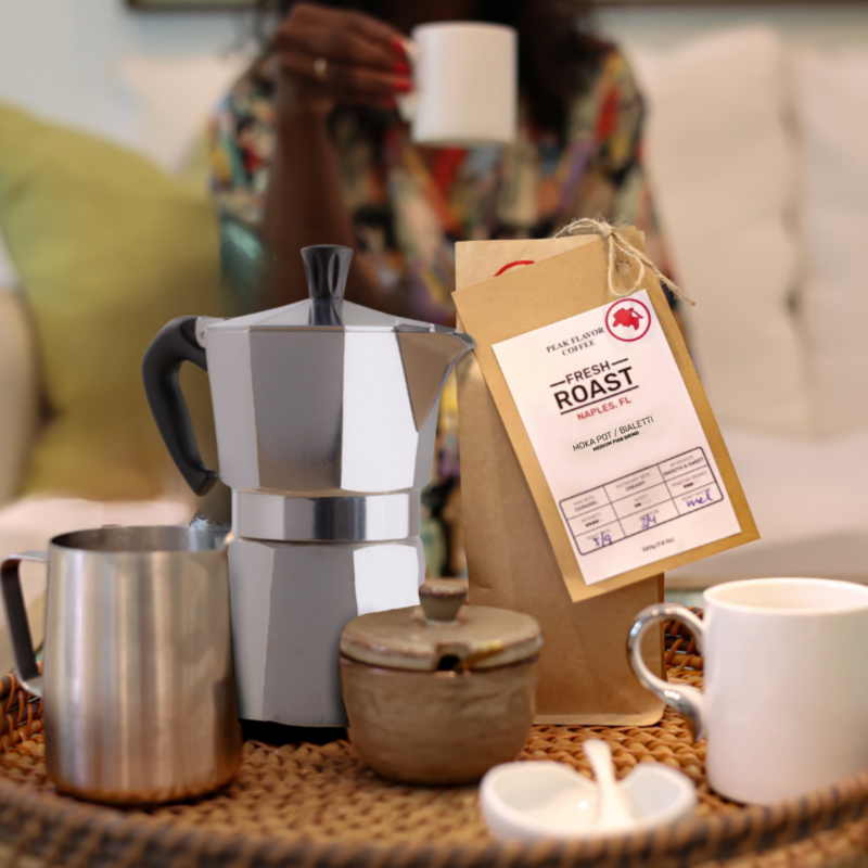 Coffee-making set with Moka pot, coffee bag, and cups on a table.