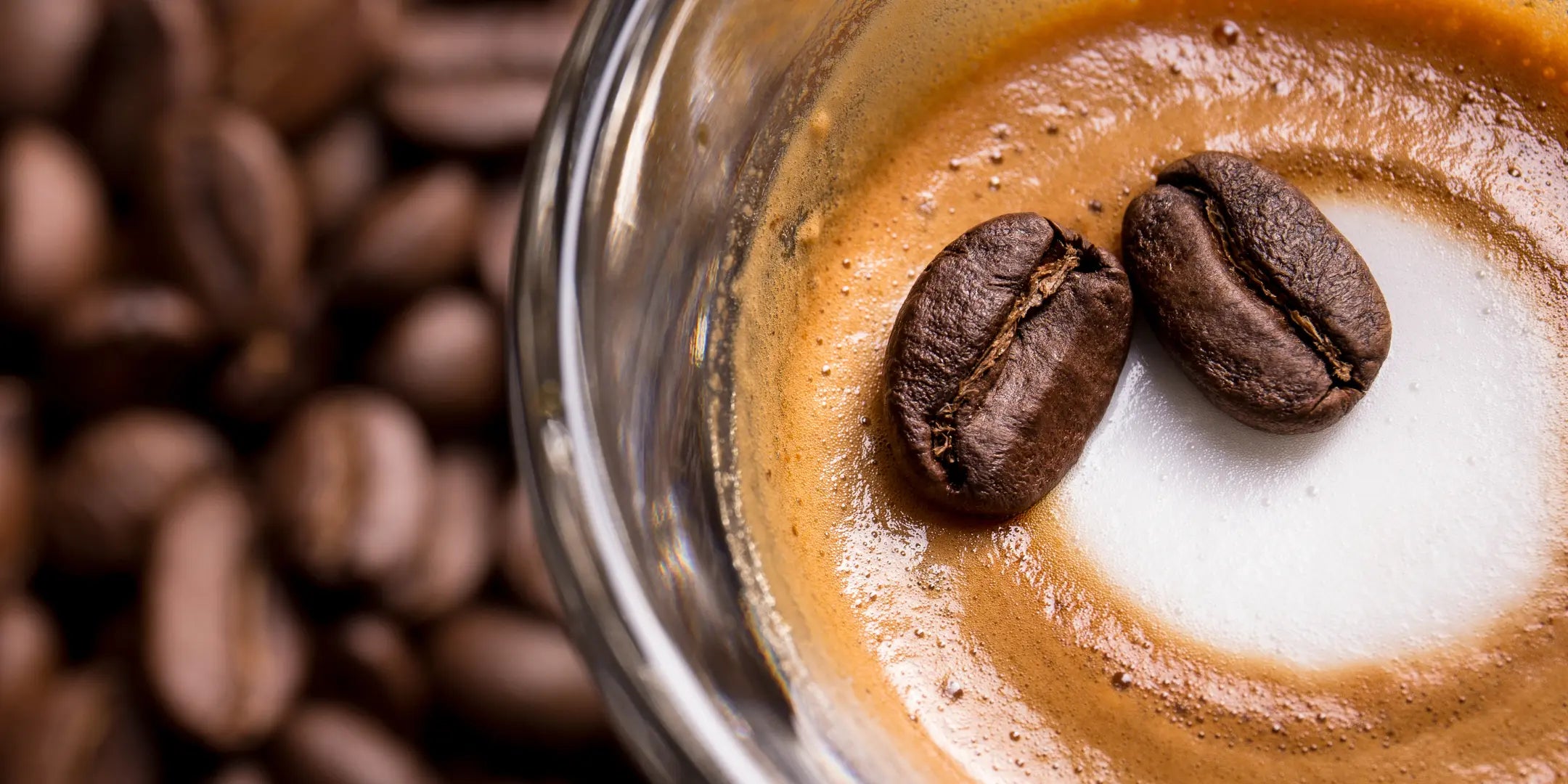 top view of espresso in a glass cup with blurred coffee beans in the background